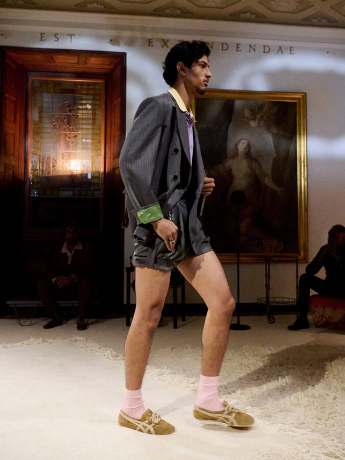 Modelo masculino desfilando con traje gris y zapatillas marrones Onitsuka Tiger x Versace