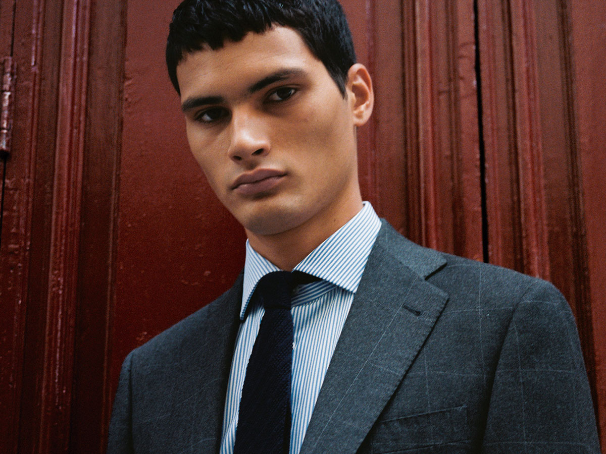 Alejo Humanes, modelo madrileño, retratado con traje y corbata frente a una puerta roja para Rísbel Magazine otoño 2025.