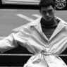 El modelo Alejo Humanes vestido con un jersey de cuello alto y una gabardina y sentado en un banco