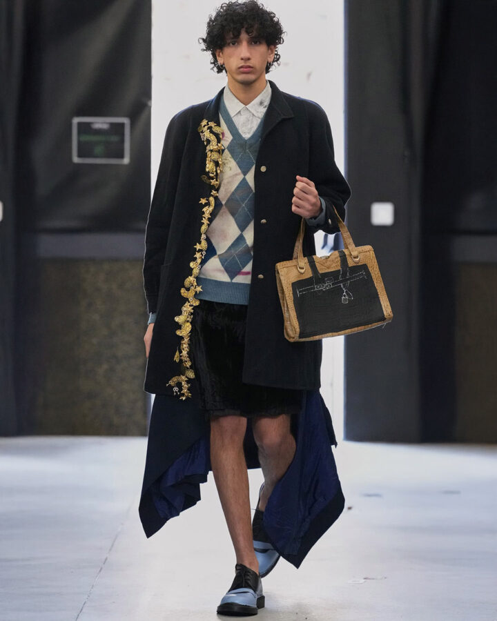 Modelo con jersey de rombos azul celeste y abrigo largo en el desfile de Simon Cracker otoño/invierno 2025.