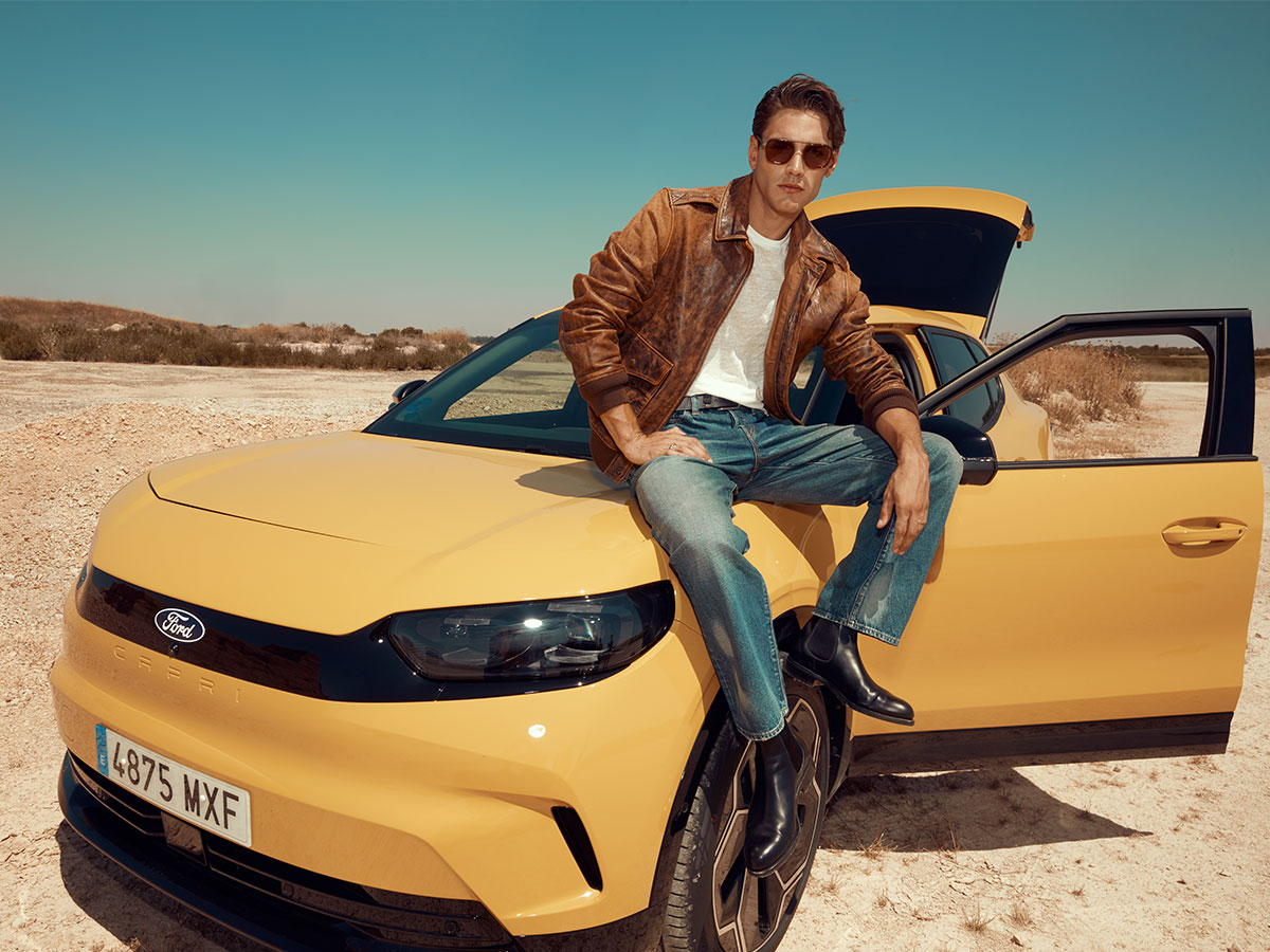 Modelo sentado sobre el capó del Ford Capri 2025 con las puertas abiertas en un paisaje desértico.
