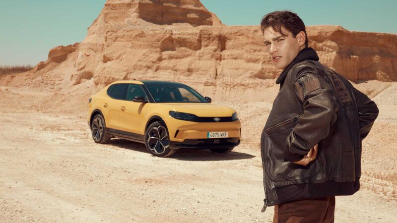 Modelo con chaqueta de aviador frente al nuevo Ford Capri 2025 en color amarillo.
