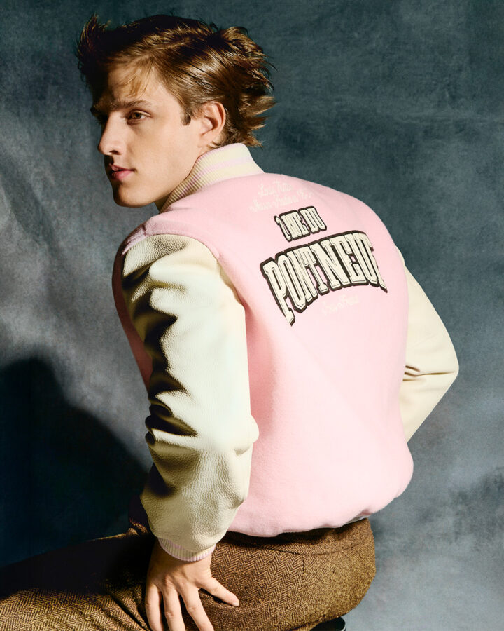 El actor Nuno Gallego sentado en un taburete de espaldas y mirando hacia el lado izquierdo, con una chaqueta Varsity rosa. Sesión de fotos realizada para Rísbel Magazine.