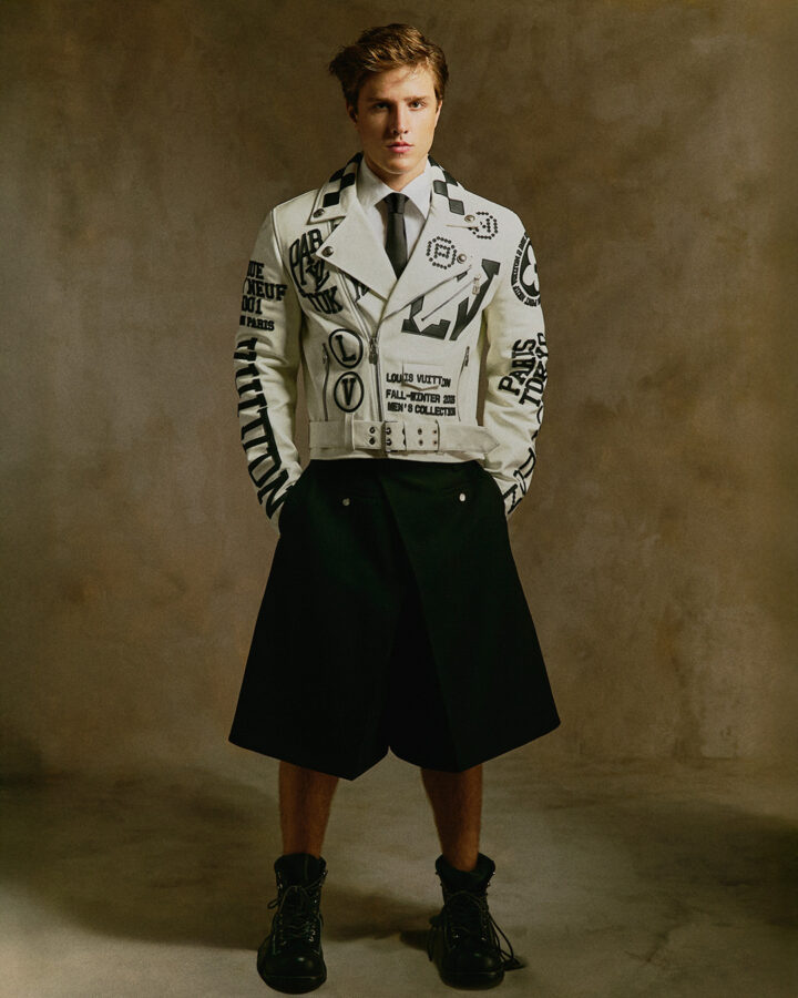 El actor Nuno Gallego de pie eun un estudio de fotografía, vestido con unas bermudas negras holgadas, una chaqueta blanca de piel, camisa y corbata. Foto realizada por la revista Rísbel para su número de otoño de 2025.