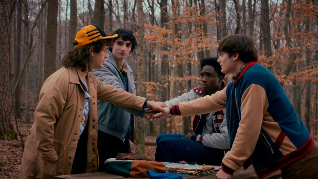 Escena de la quinta temporada de la serie Strangers Things de Nteflix, en la que se ve a la pandilla de amigos uniendo las manos en un bosque