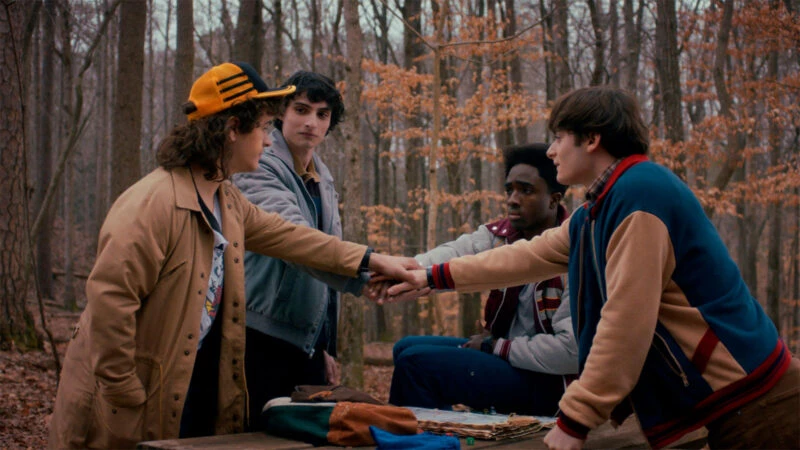 Escena de la quinta temporada de la serie Strangers Things de Nteflix, en la que se ve a la pandilla de amigos uniendo las manos en un bosque