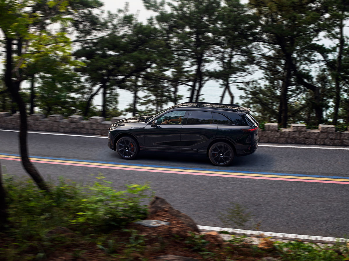 Xpeng G9 2025 circulando por carretera junto al mar rodeado de árboles.