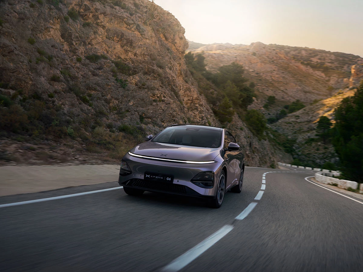 XPENG G6 en movimiento por una carretera de montaña al atardecer, mostrando su frontal con faros LED “Starlight”.