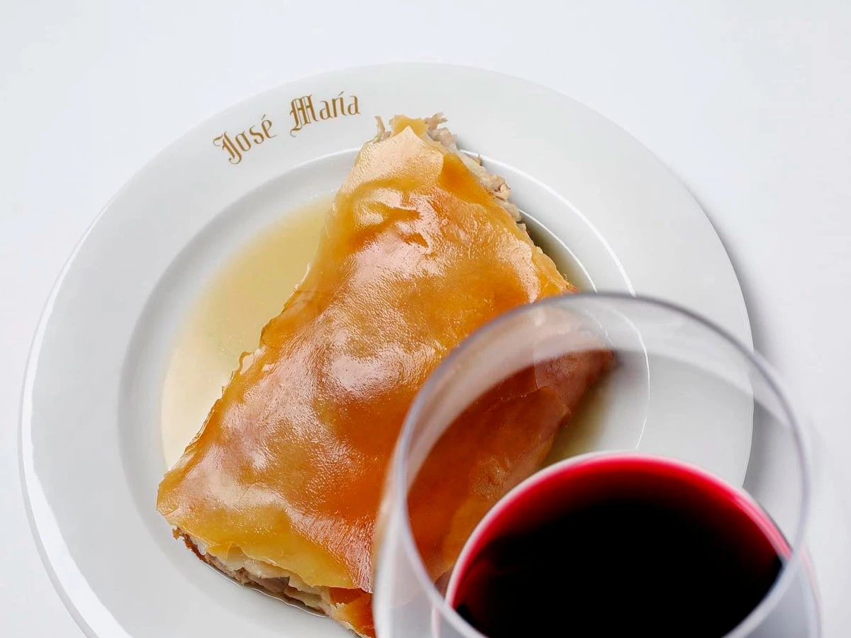Ración de cochinillo asado del restaurante José María acompañada de una copa de vino tinto.