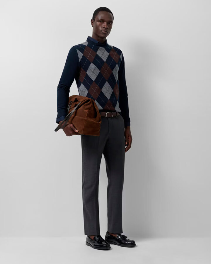 Hombre con jersey de rombos azul marino, gris y marrón de Roberto Verino, look formal con pantalón gris y bolso de ante marrón.