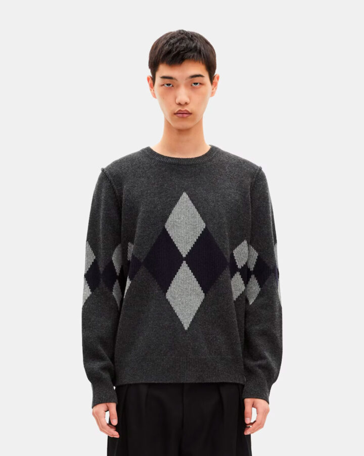 Modelo con jersey de rombos grises y azul marino de The Kooples, combinado con pantalones negros amplios.