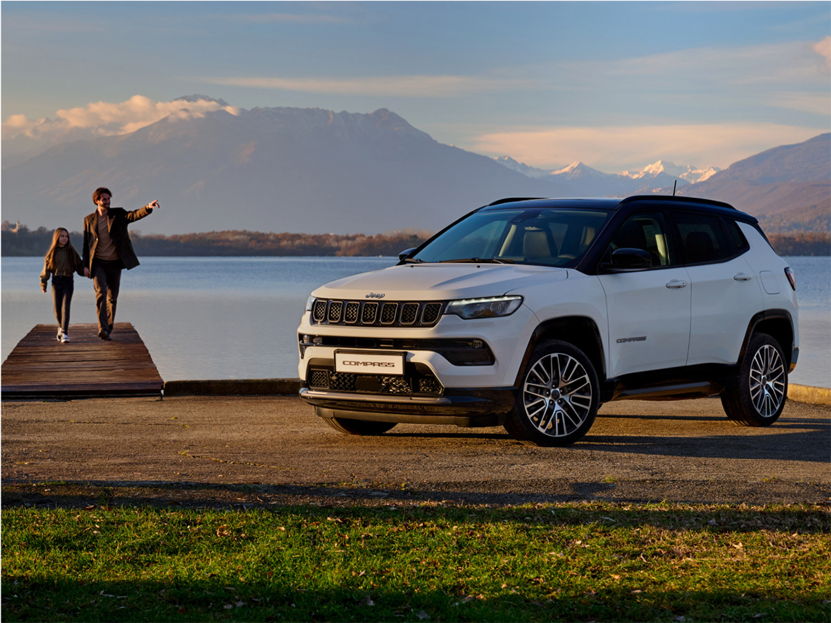 Fotografía de un Jeep Compass 4xe aparcado frente a un muelle y un lago con un padre cogiendo de la mano a su hijo y señalando al horizonte.