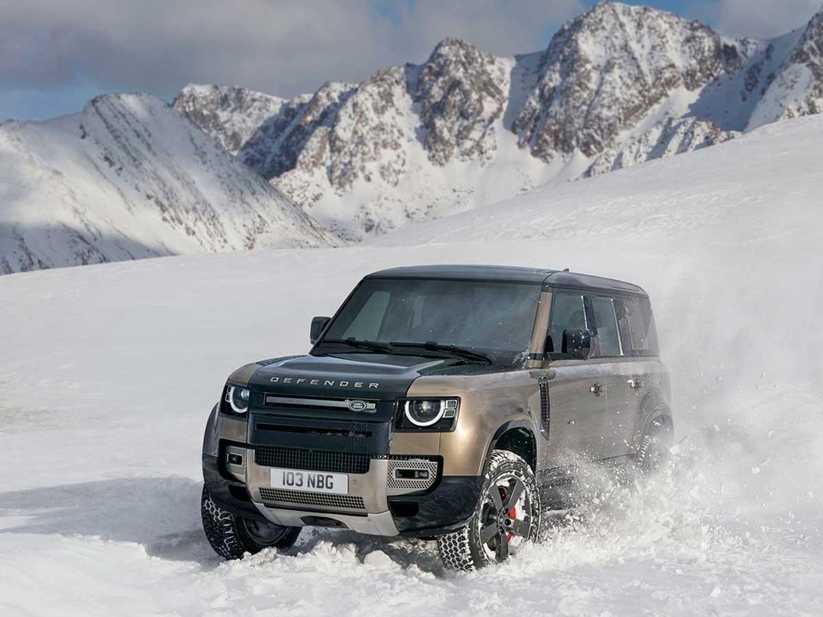 Coche Land Rover Defender 110 conducido por mitad de una montaña muy nevada