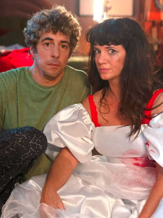 Escena de la serie "Envidiosa" en la que se ve a la protagonista vestida de novia sentada en el suelo de su habitación junto a su pareja.