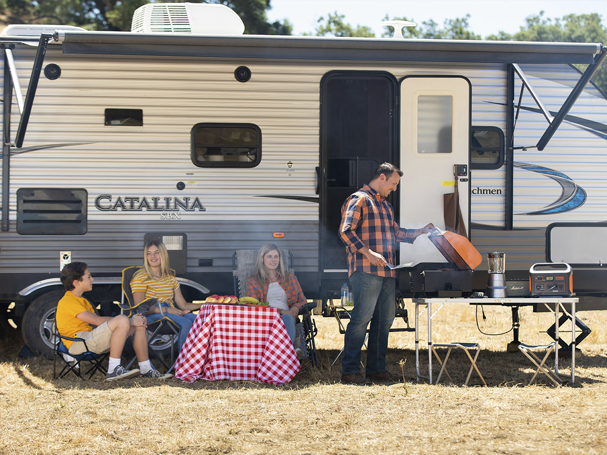 Caravana aparcada y una familia haciendo una barbacoa fuera