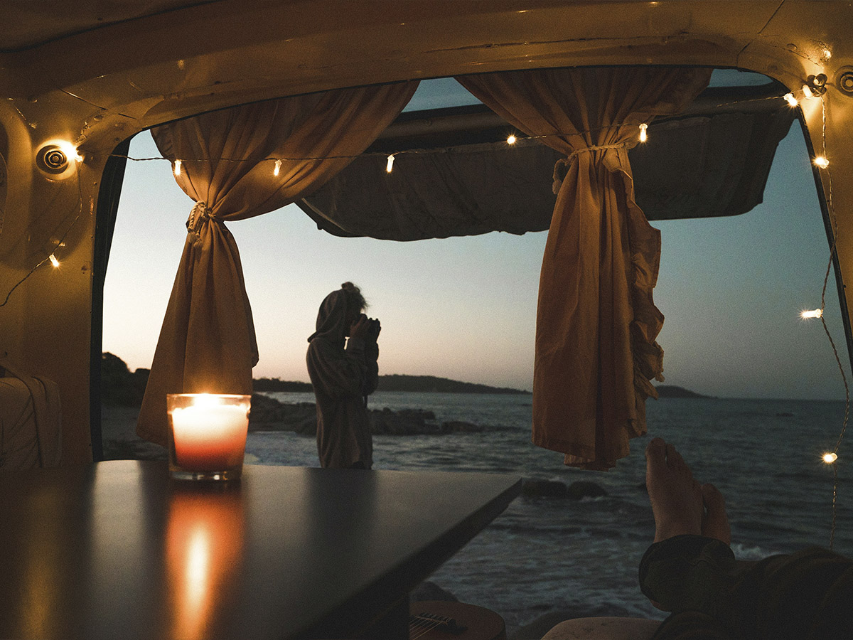 Una pareja se da un beso en un atardecer y la foto está tomada desde el interior de una caravana con vistas a un acantilado
