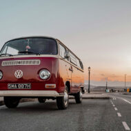 Autocaravana volkswagen clásica roja estilo años 70 aparcada en una carretera al atardecer