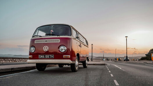 Autocaravana volkswagen clásica roja estilo años 70 aparcada en una carretera al atardecer