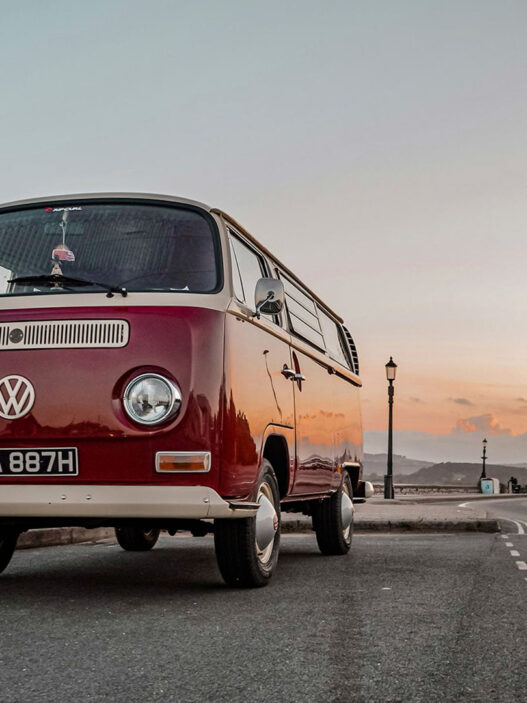 Autocaravana volkswagen clásica roja estilo años 70 aparcada en una carretera al atardecer