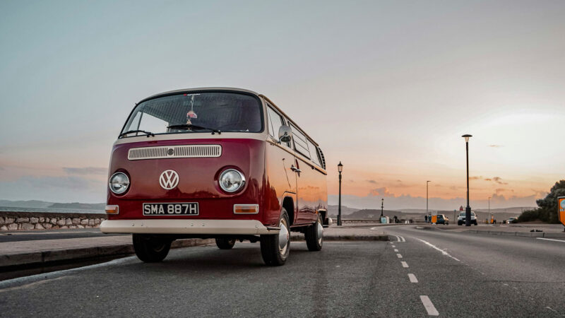 Autocaravana volkswagen clásica roja estilo años 70 aparcada en una carretera al atardecer