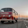 Autocaravana volkswagen clásica roja estilo años 70 aparcada en una carretera al atardecer