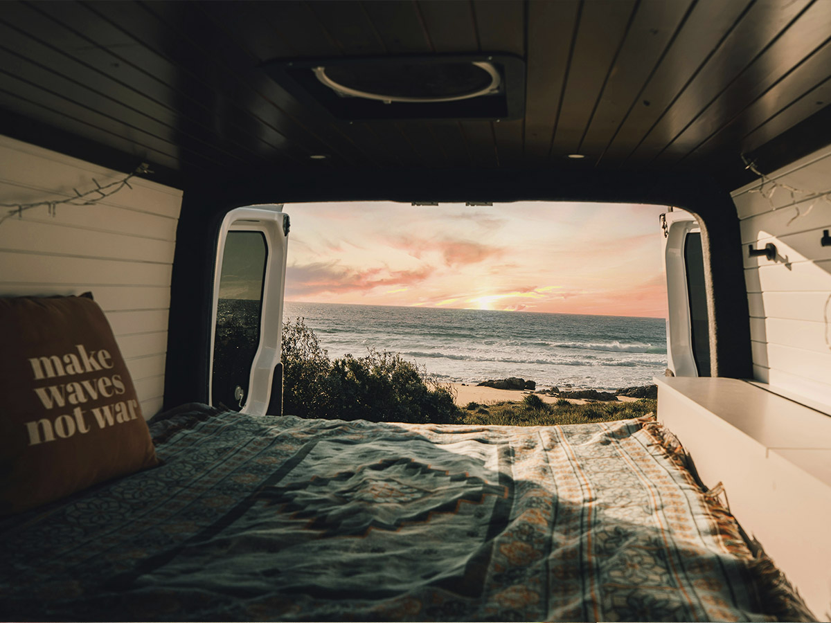 Parte trasera de una autocaravana con vistas a una playa amaneciendo.
