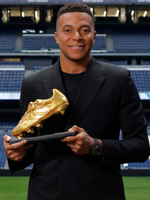 Kylian Mbappé posando con la Bota de Oro 2025 vestido con un traje negro de Dior.