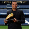 Kylian Mbappé posando con la Bota de Oro 2025 vestido con un traje negro de Dior.