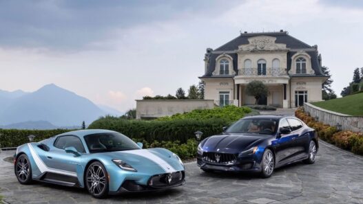 Dos coches de lujo de la maca Maserati, ambos de color azul, aparcados en un jardín frente a una casa muy elegante en un día nublado.