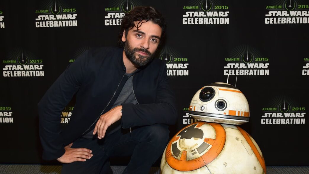 Fotografía del actor Oscar Isaac apoyado sobre una maqueta del robot R2D2 en una presentación de Star Wars.