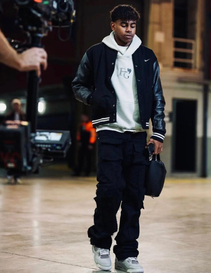 Lamine Yamal con chaqueta varsity negra, sudadera EG y pantalones cargo oscuros.