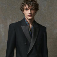 Zara acaba de sacar un traje estilo esmoquin edición limitada que se va a convertir en el imprescindible de tus cenas de gala esta Navidad 2025 Modelo masculino con traje negro de doble botonadura, apoyado en un taburete alto en un entorno minimalista de tonos grises.