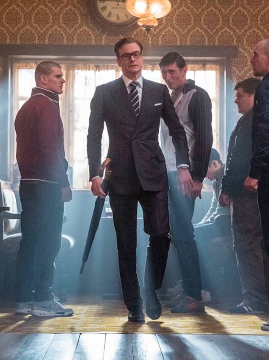 Escena de la película Kingsman: El servicio secreto, en la que se ve Colin Firth vestido de traje muy elegante entrando a un bar en el que hay chicos vestidos informales