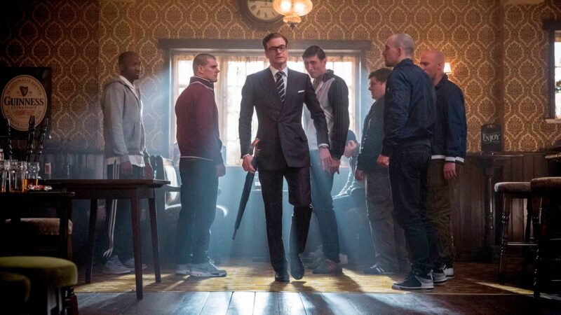 Escena de la película Kingsman: El servicio secreto, en la que se ve Colin Firth vestido de traje muy elegante entrando a un bar en el que hay chicos vestidos informales