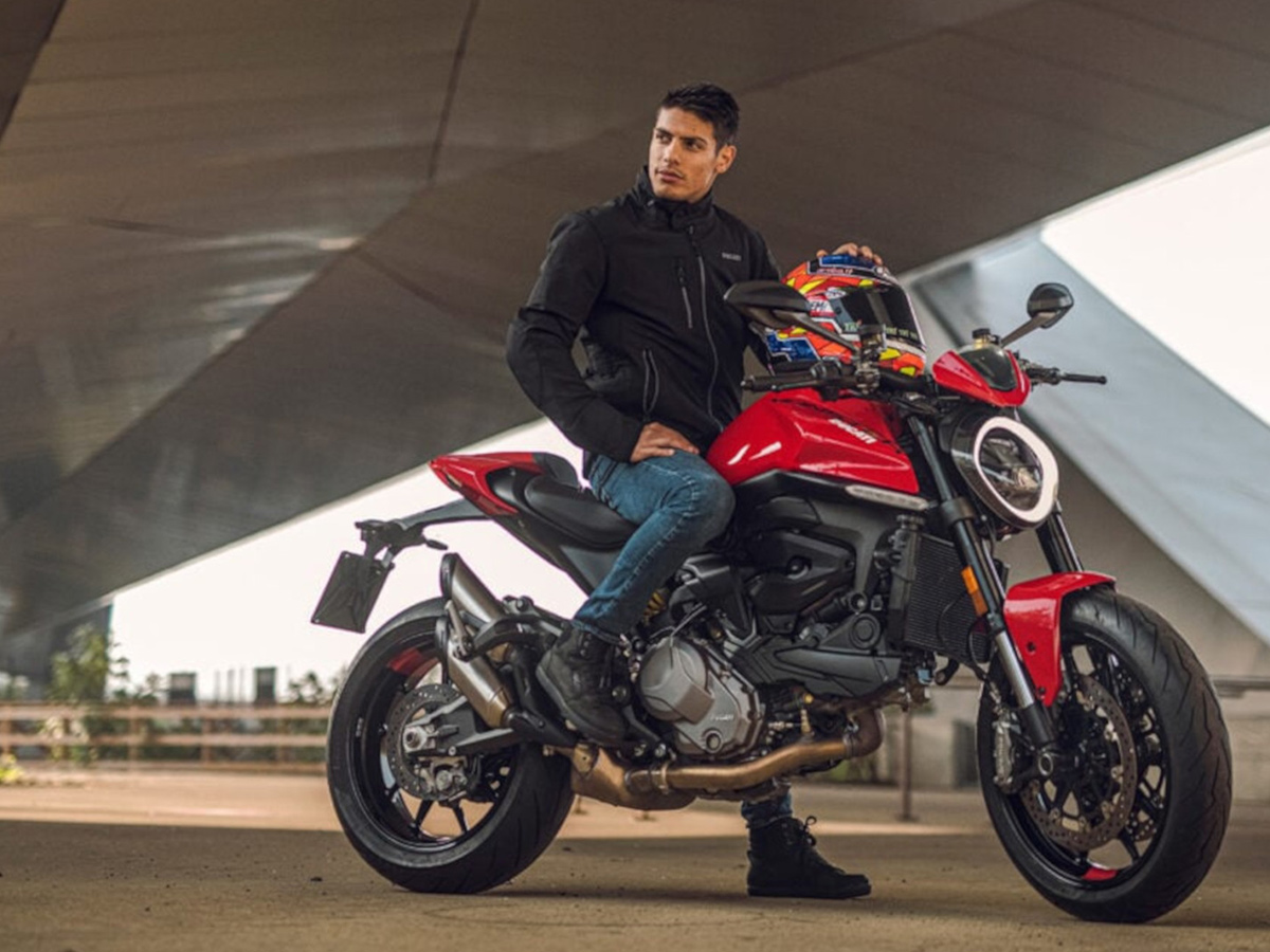 Chico joven posa con su moto para y el casco en la mano.