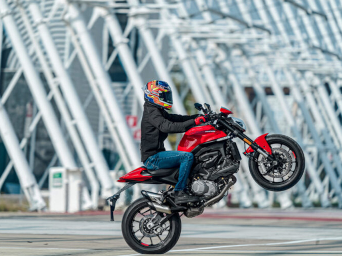 Hombre haciendo un caballito encima de una Ducati Monster roja