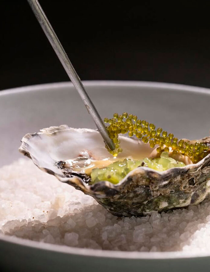 Ostra con kiwi y sansho del restaurante Tetsu, presentada sobre una base de sal marina.