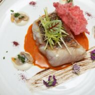 Probamos la nueva carta del restaurante Zalacaín y descubrimos por qué es el lugar favorito de la cúpula del Real Madrid Plato de Suprema de mero con salsa de chiote, ajonegro, berberechos y crujiente de hibiscus del restaurante Zalacaín de Madrid