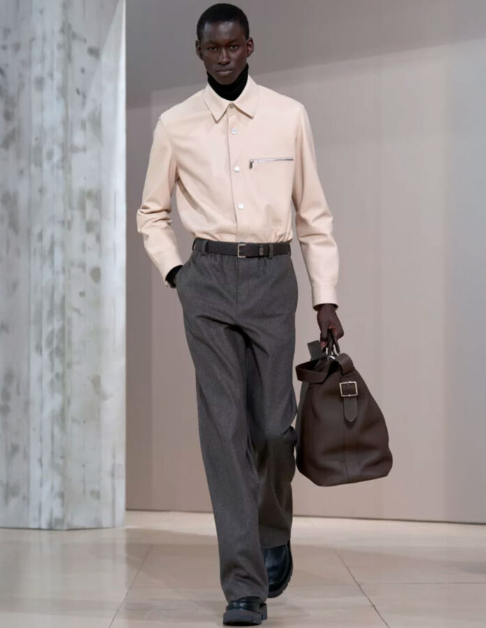 Look de Hermès otoño-invierno 2025 con camisa crema sobre jersey negro de cuello alto y pantalón de pinzas gris.