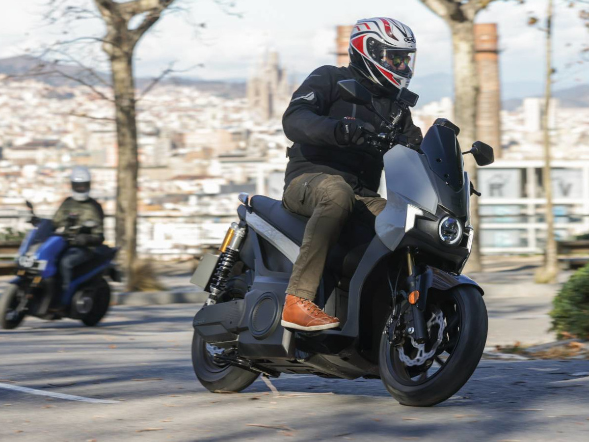 Conductor pilotando un SEAT MÓ 125 gris en una carretera urbana.
