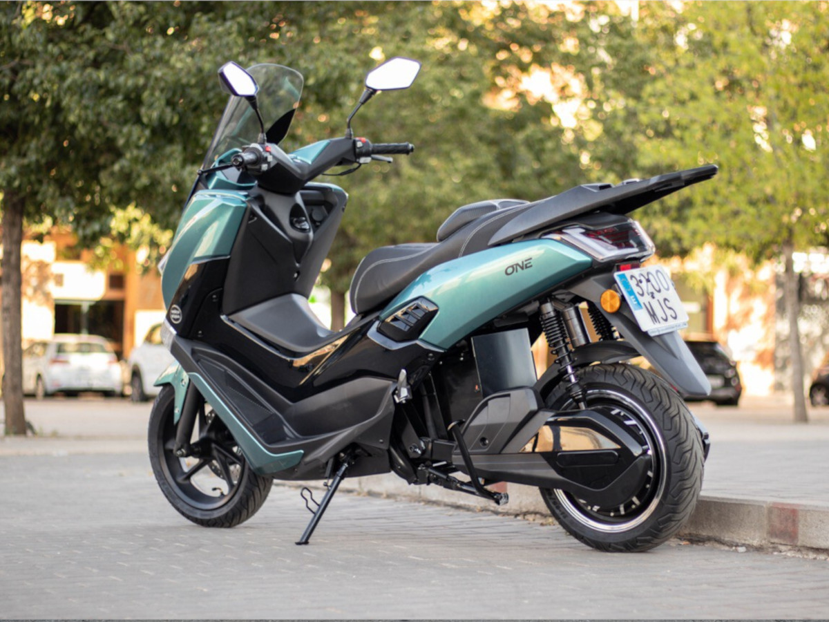 Scooter Velca One en color verde, aparcado en un entorno urbano arbolado.