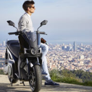 5 scooters eléctricos de 125 que tienes que tener en el radar para aprovechar al máximo los descuentos del Plan Moves III antes de que termine hombre apoyado en un scooter de 125 eléctrico mirando al horizonte en un mirador sobre una ciudad