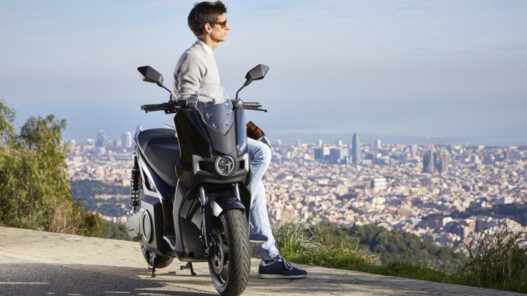 hombre apoyado en un scooter de 125 eléctrico mirando al horizonte en un mirador sobre una ciudad