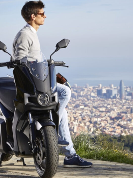 hombre apoyado en un scooter de 125 eléctrico mirando al horizonte en un mirador sobre una ciudad