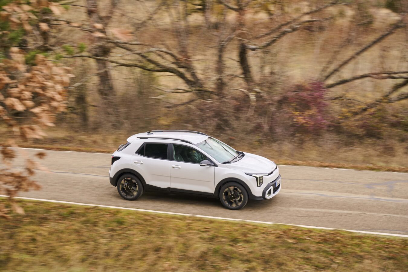 Kia Stonic 2025 facelift en blanco, vista lateral circulando con llantas de aleación y barras de techo