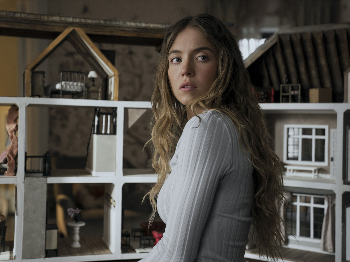 Escena de la película La Asistenta, en la que aparece Sydney Sweeney en una haitación, frente a una casita de muñeca mirando para atrás con rostro preocupado.