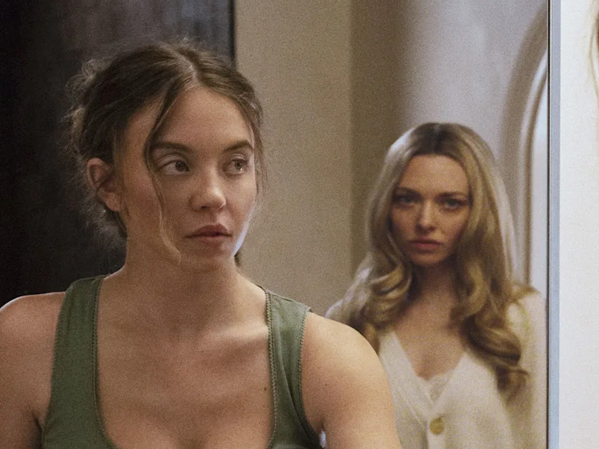 Escena de la película La Asistenta, en la que aparece Sydney Sweeney mirando a través de un espejo a Amanda Seyfried, que se encuentra tras ella, con rostro de incertidumbre.