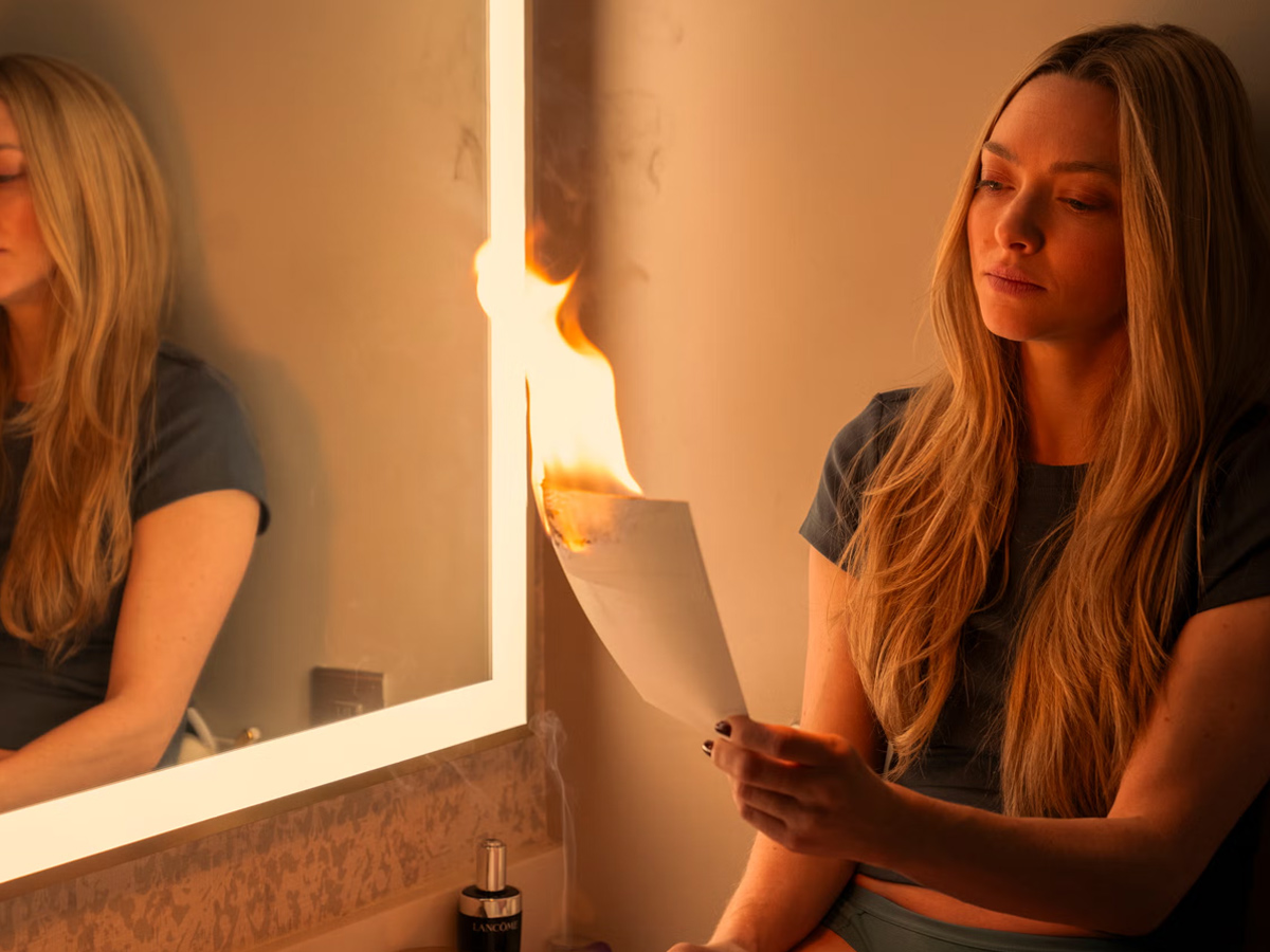 Escena de la película La Asistenta, en la que aparece Amanda Seyfried mirando arder un folio que sostiene ella misma en la mano con rostro de tranquilidad o alivio.