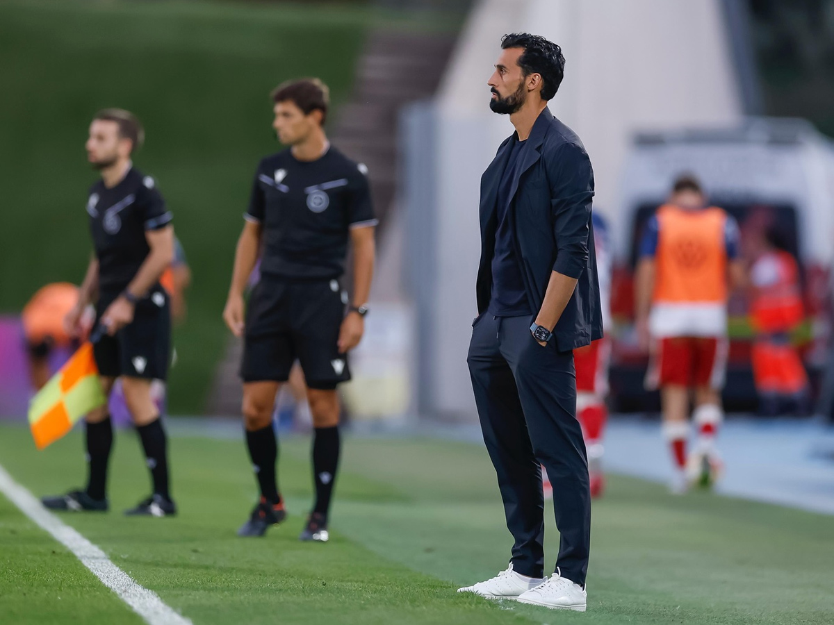 Álvaro Arbeloa en la banda durante un partido con traje oscuro técnico y zapatillas blancas