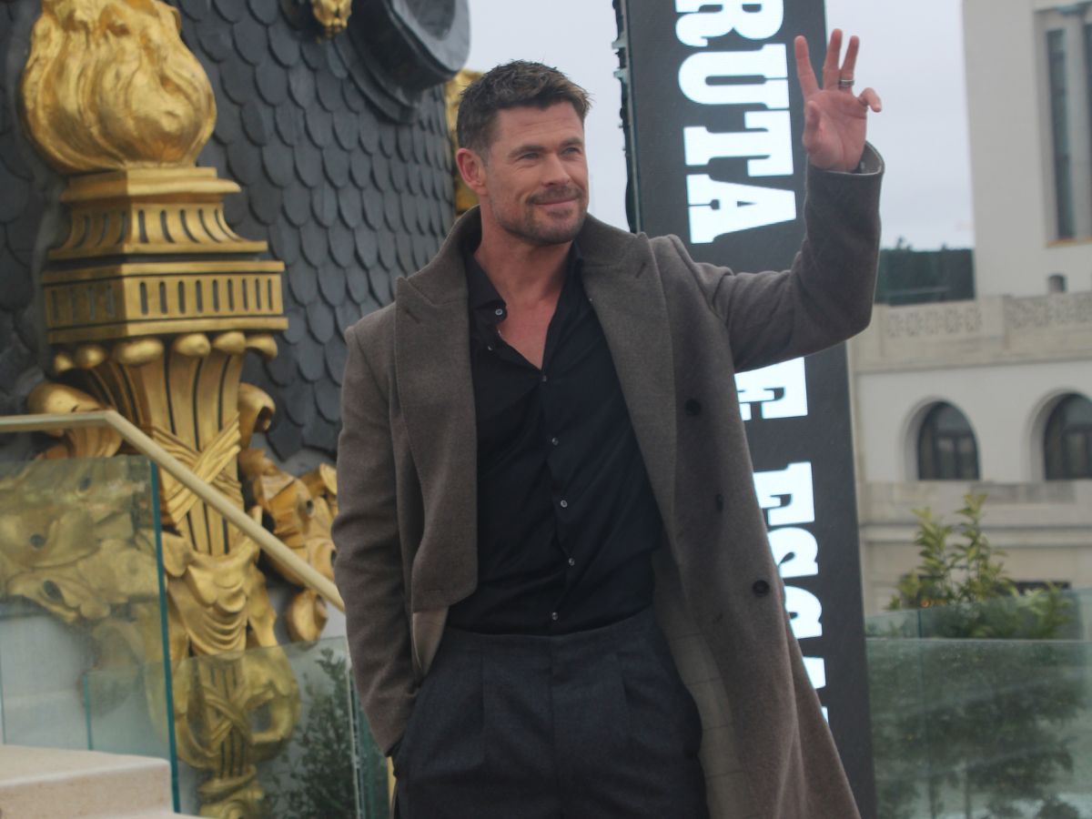 Chris Hemsworth con un abrigo gris, camisa negra y pantalón gris saludando a los fotógrafos en Madrid.